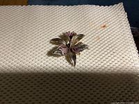 Front view of orchid brooch showing silver-toned metal petals with pink accents on petals and visible details of flower shape.