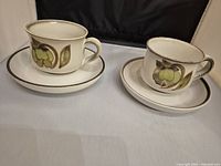 Pair of Denby cups and saucers, cream color with floral designs featuring green and brown colors, rims darker speckled brown edge.