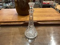Clear crystal decanter with pinwheel cut pattern standing on a reflective surface with wooden background.