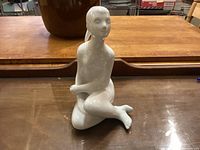Front view of white porcelain nude figurine sitting with legs and arms crossed, smooth glossy finish