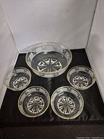 Set of one large bowl and four small bowls arranged on black fabric showing gold rim and fleur-de-lis decoration.