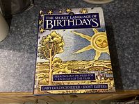 Front cover of 'The Secret Language of Birthdays' showing title, authors, and colorful illustration of sun, tree, and landscape.