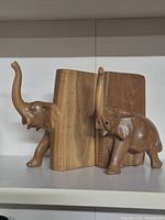 Wooden elephant bookends positioned on a shelf with books between them, showing their side and front view.