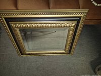 Rectangular wooden framed mirror with ornate gold molding and black accent strip, showing reflective glass surface.
