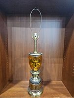 Full view of the vintage amber glass and brass table lamp without the shade attached, showing the harp and brass fittings.