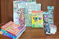 Lot arranged on table showing adult coloring books, word-find books, markers, colored pencils, stickers, and card holders