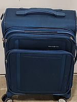 Closed blue Samsonite soft side suitcase showing front zippered compartments and durable fabric.
