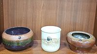 Three ceramic pots side by side on wooden shelf showing overall appearance and colors