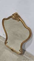 Front angle of the vintage handcrafted gold wall mirror showing decorative scroll and shell motifs on top frame.