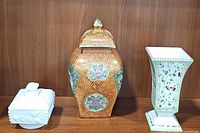 Photo of the three items in the lot: lidded orange decorative jar in center, Westmoreland beaded grape milk glass honey box on left, ceramic floral pedestal vase on right.