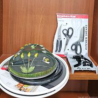 Full view of various kitchen gadgets showing vintage food cover, KitchenAid shears in package, wine opener, and turntables stacked