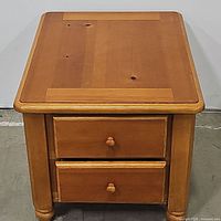 Front view of pine nightstand, showing top and both closed drawers with wooden knobs.