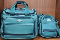 Front view of both the large rolling luggage and smaller carry bag side by side showing fabric texture and logos