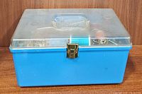 Closed blue sewing box with clear lid and gold-colored latch, plastic handle on top.