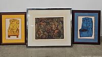 Three framed tribal art prints arranged side by side: left print in yellow matte and light wood frame, center print in chrome frame signed Caporaso 1964, right print in blue matte and dark wood frame.