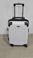 Front view of the white hard-shell spinner suitcase showing the protective black corner guards and telescoping handle.