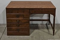 Front view of wooden desk showing four stacked drawers on the left, two smaller drawers on top, turned leg supports on the right, and flat wooden desktop.