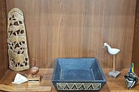 Shelf display including African carved panel, black carved box, folk pottery bird, carved wooden bird, and Bermuda onion statue with label