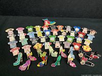Top-down photo showing an assortment of Disney character shirt-shaped pins and shoe-shaped pins spread out in rows on black background.