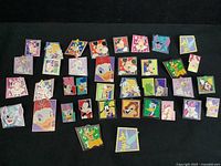 Top-down view of 42 Disney square character trading pins laid out on black surface, showing various Disney characters in colorful square frames.