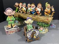 Front view of two Dopey figurines and the seven dwarfs on log against black background.