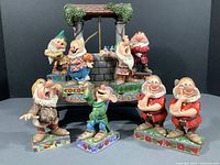 Frontal shot of eight dwarf figurines arranged around the wishing well stand on a black display area