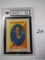 Front side of 1970-71 O-Pee-Chee Jean Ratelle sticker stamp graded 6.5 EMN+. Shows Jean Ratelle in New York Rangers jersey with yellow and orange background.