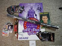 Photo showing a collection of basketball memorabilia including Vince Carter and Stacey King posters, trading cards, Bob Cousy book, Scottie Pippen item, and figurines on carpet.