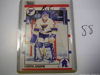 Front of Curtis Joseph 1990-91 Score Rookie Card #151 in clear plastic holder, shows player with blues uniform in goalie position.