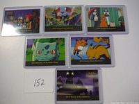 Overall view of 6 pokemon cards with blue logo in protective sleeves, showing artwork and titles including Bulbasaur and the Hidden Village, Electric Shock Showdown, Mystery at the Lighthouse
