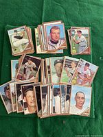 Photo showing multiple stacks and groups of 1962 Topps baseball cards laid out on a green surface, various players visible with colorful borders.