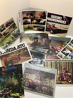 Photo showing multiple ATV dealership brochures featuring Suzuki Quadrunners, Honda ATC, and Yamaha models.