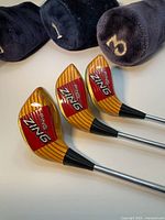 Three Ping Zing wood club heads face-up with plush headcovers marked 1, 3, 5 behind