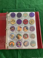 Photo of a binder page with 20 pogs featuring various designs including purple, yellow, and red tones and Lion King characters.