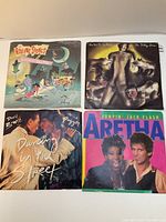 Four vinyl 45 RPM singles including two by The Rolling Stones, one by David Bowie & Mick Jagger, and one by Aretha Franklin, all with cover sleeves.