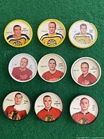 Photo showing all 9 Shirriff hockey coins laid out on a green background, arranged in 3 rows with players from Boston Bruins, Detroit Red Wings, and Chicago Blackhawks.