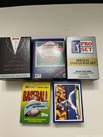 Top down image showing five sealed or boxed sports card sets of hockey, football, golf and baseball