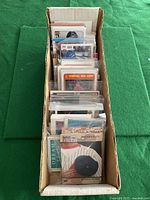 Top view of a long box filled with assorted sports cards in plastic sleeves, showing front cards featuring baseball players.