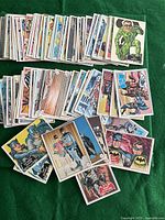 Photo showing a large spread of Batman vintage cards laid out on a green surface, displaying various characters like Batman, Robin, the Riddler, and others.
