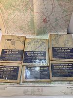 Seven vintage fishing and hunting maps arranged on a surface with one map opened in the back revealing a large grid and several red points.