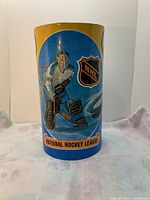 Front side showing NHL goalie and NHL logo on blue background with yellow top rim