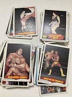 Photo showing multiple stacks of WWF wrestling cards from the 1980s. Cards show action poses and wrestlers including Leilani Kai and others with colorful comic-style captions.