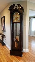Full front view of mahogany grandfather clock showing bonnet, dial and base