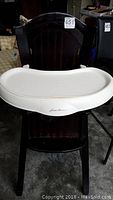 Front view of the dark painted wooden high chair with white plastic tray attached and marked Eddie Bauer.