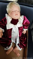 Full front view of Lee Middleton doll dressed in red velveteen onesie with lace and satin bow