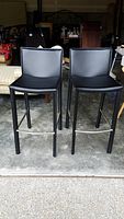 Front view of two black low back bar stools with faux leather seats and black metal legs, placed side by side.