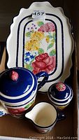 Photo showing tea pot, sugar bowl, milk jug on a tea tray with floral patterns in blues, pinks, yellows and greens