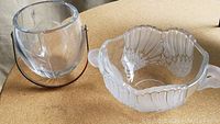 Two crystal bowls on a wooden surface, one clear with metal handle, one oval with frosted wing pattern