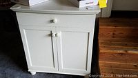 Front view of cream painted vanity cabinet with two doors and drawer on wooden floor.