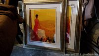 Two framed prints stacked, showing a woman in a red dress in foreground and another print behind.
